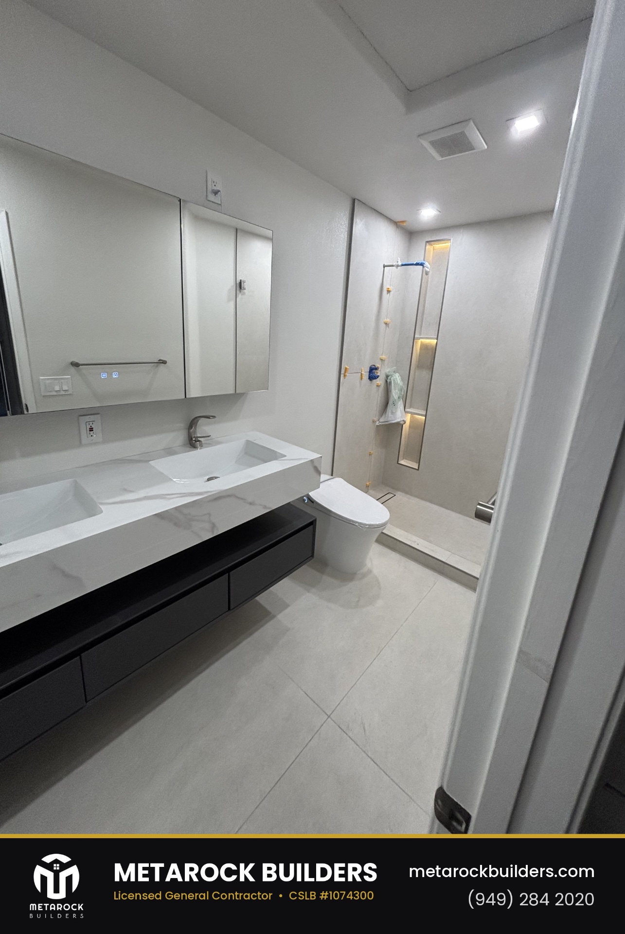 Bathroom and shower remodel in Orange County by Metarock Builders, completed after photo with floating double-sink marble vanity, black cabinetry, integrated medicine cabinet, and micro-cement walk-in shower with lit niche