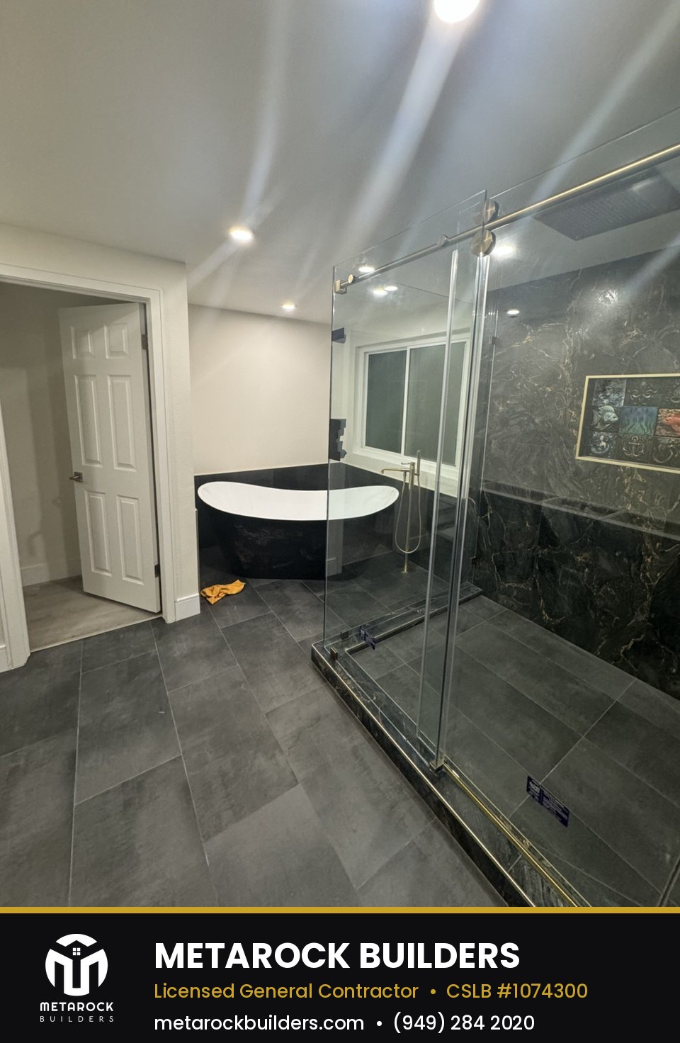 Bathroom remodel in Orange County by Metarock Builders, completed after photo with dark marble-look tile, freestanding tub, and frameless glass shower with brushed brass hardware