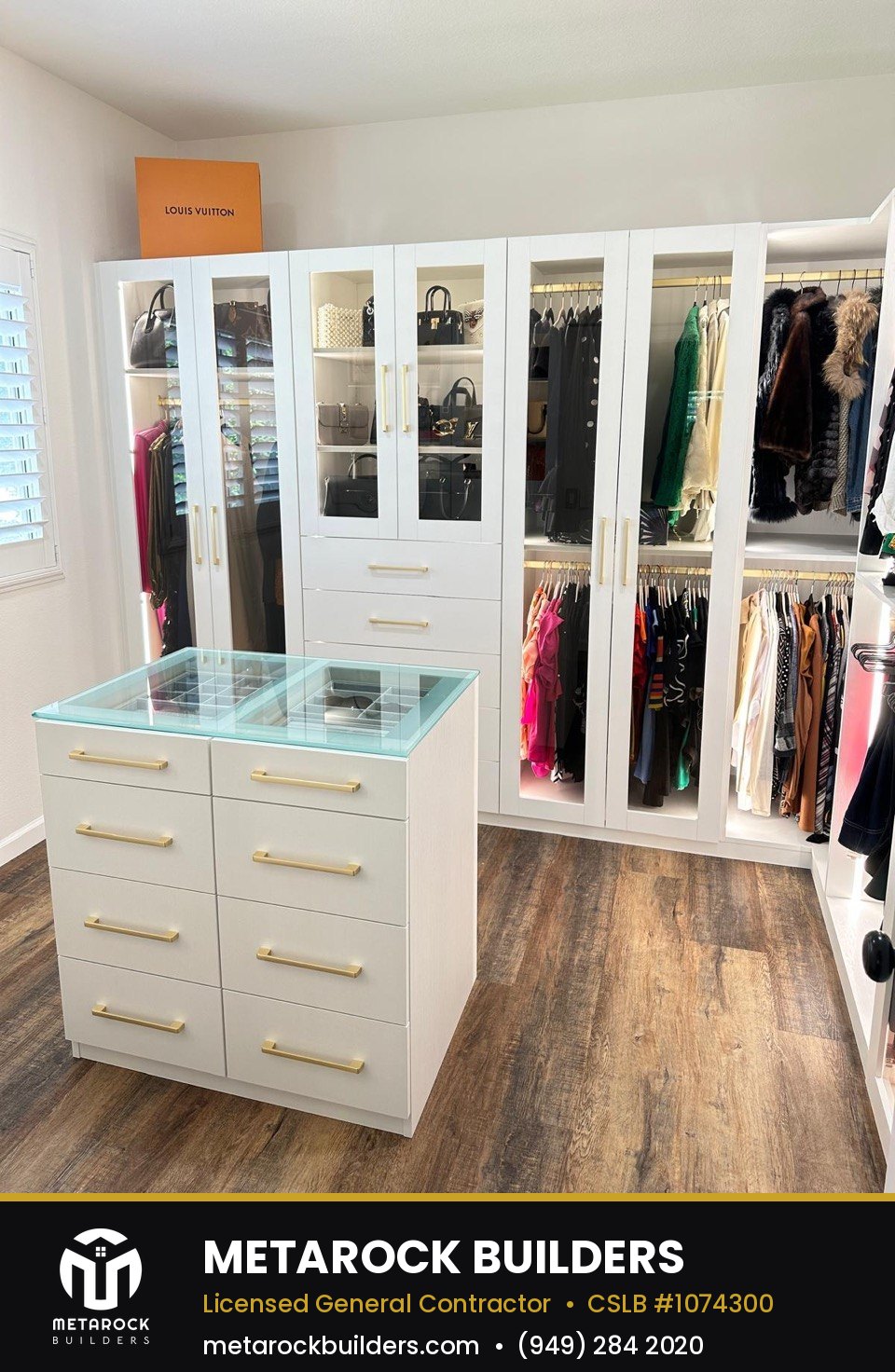Closet remodel in Orange County by Metarock Builders, completed after photo with full-wall wardrobe system, glass-front cabinets, and center island with glass top