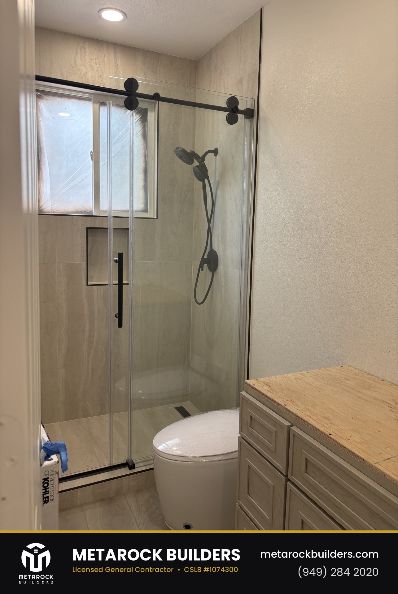 Shower remodel in Orange County by Metarock Builders, completed after photo with travertine-look tile walls, frameless sliding glass door, matte black hardware, and built-in niche
