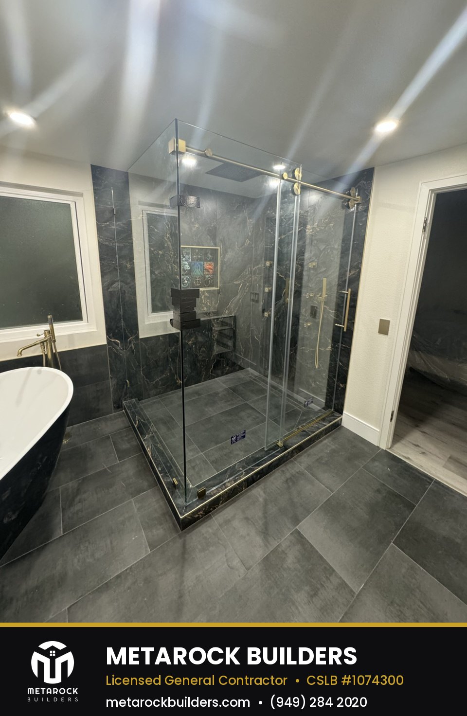 Bathroom remodel in Orange County by Metarock Builders, completed after photo with book-matched black marble shower walls, brushed brass fixtures, built-in niche, and frameless glass enclosure