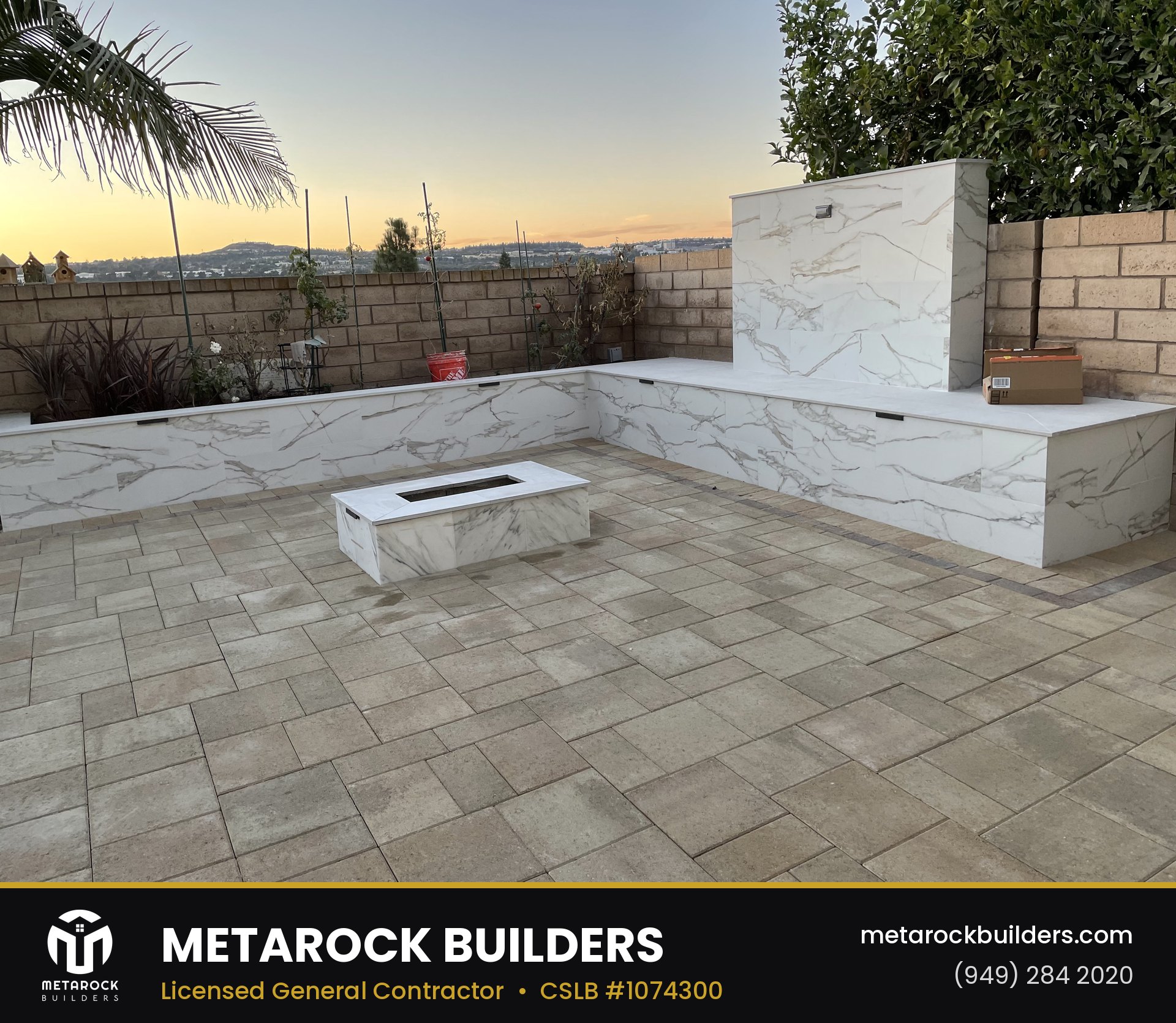 Paver patio in Orange County by Metarock Builders, completed after photo with gray stone pavers, marble-clad built-in bench seating, marble fire feature, and linear gas fire pit at sunset