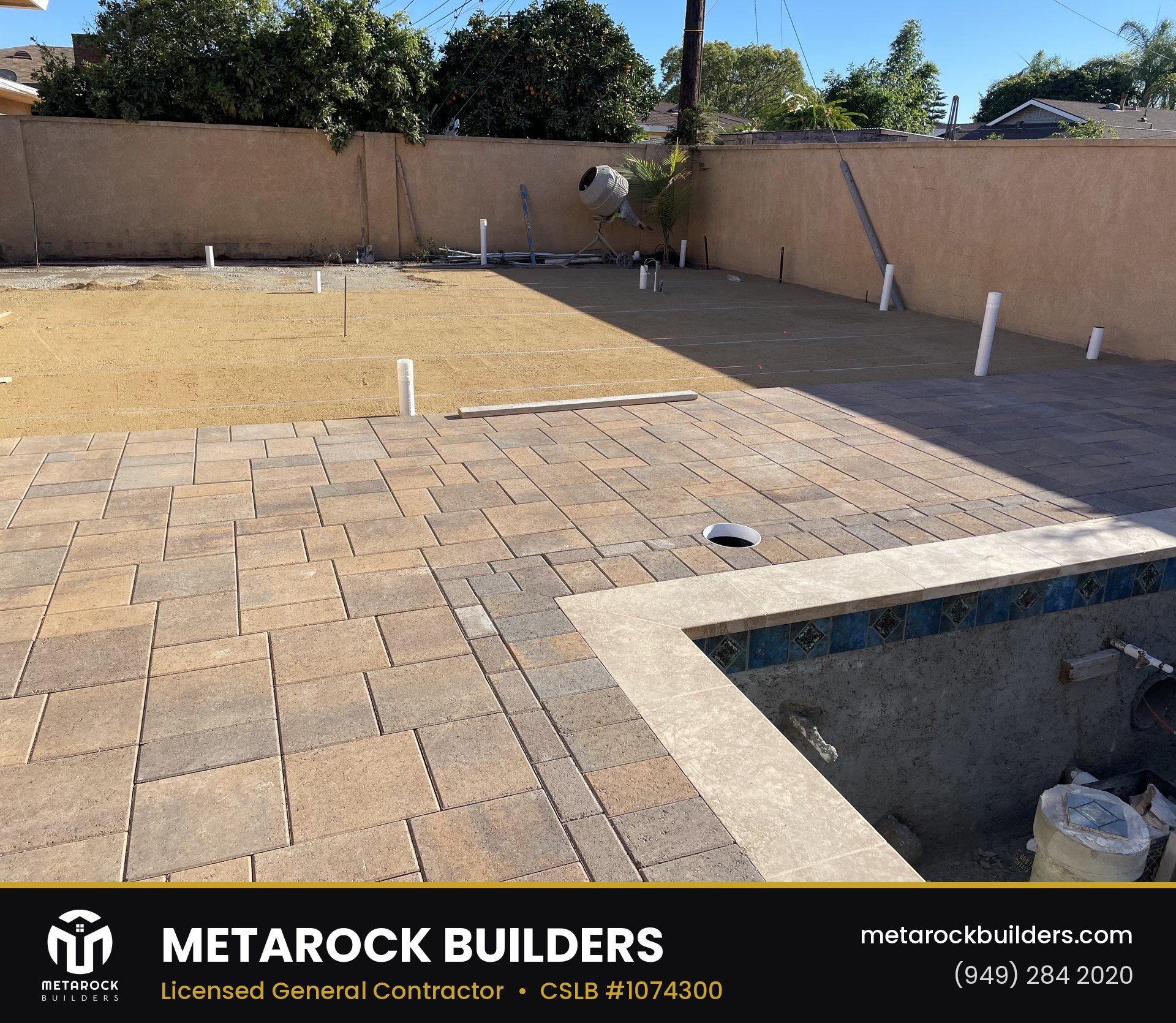 Paver patio and pool deck in Orange County by Metarock Builders, in-progress photo with warm-tone stone pavers in basketweave pattern, travertine pool coping, and mosaic tile pool waterline
