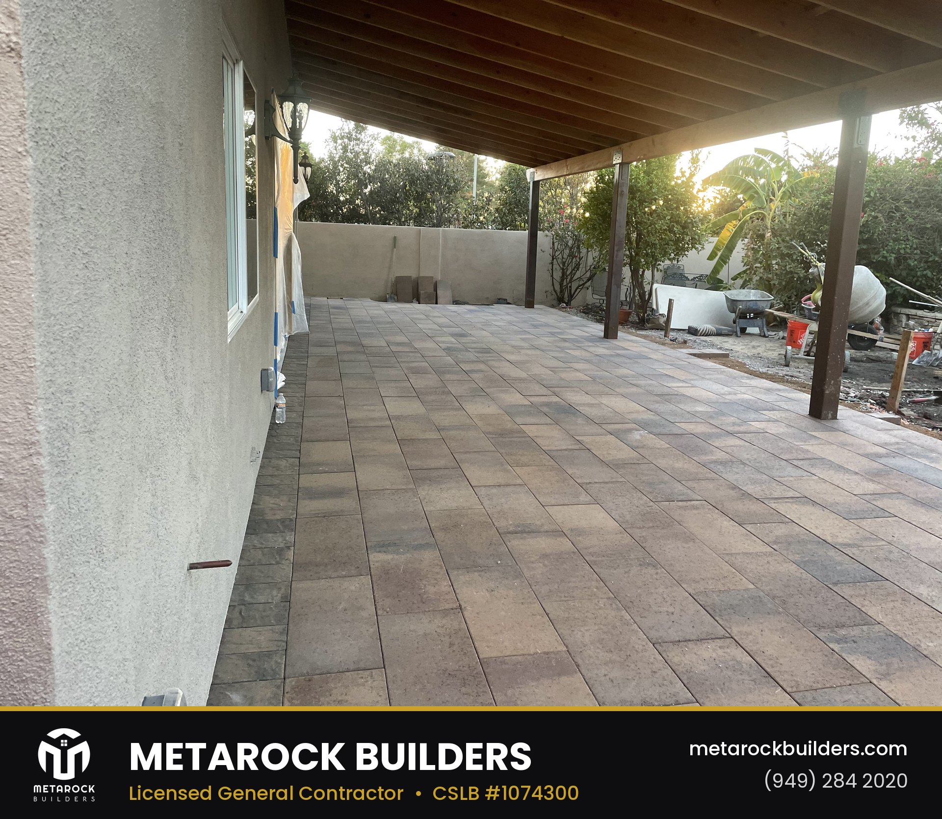 Paver patio in Orange County by Metarock Builders, completed after photo with warm-tone stone pavers under a wood patio cover