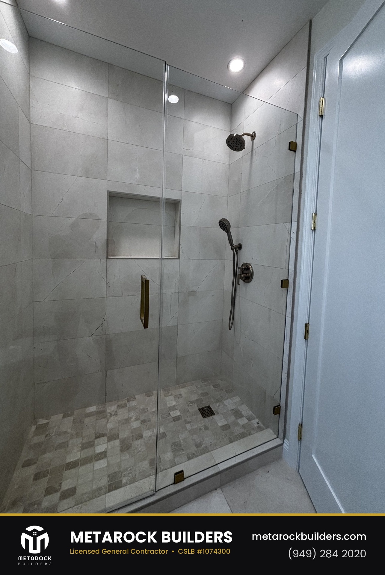 Shower remodel in Orange County by Metarock Builders, completed after photo with large-format marble-look tile walls, frameless glass enclosure, brushed brass hardware, built-in niche, and stone mosaic floor