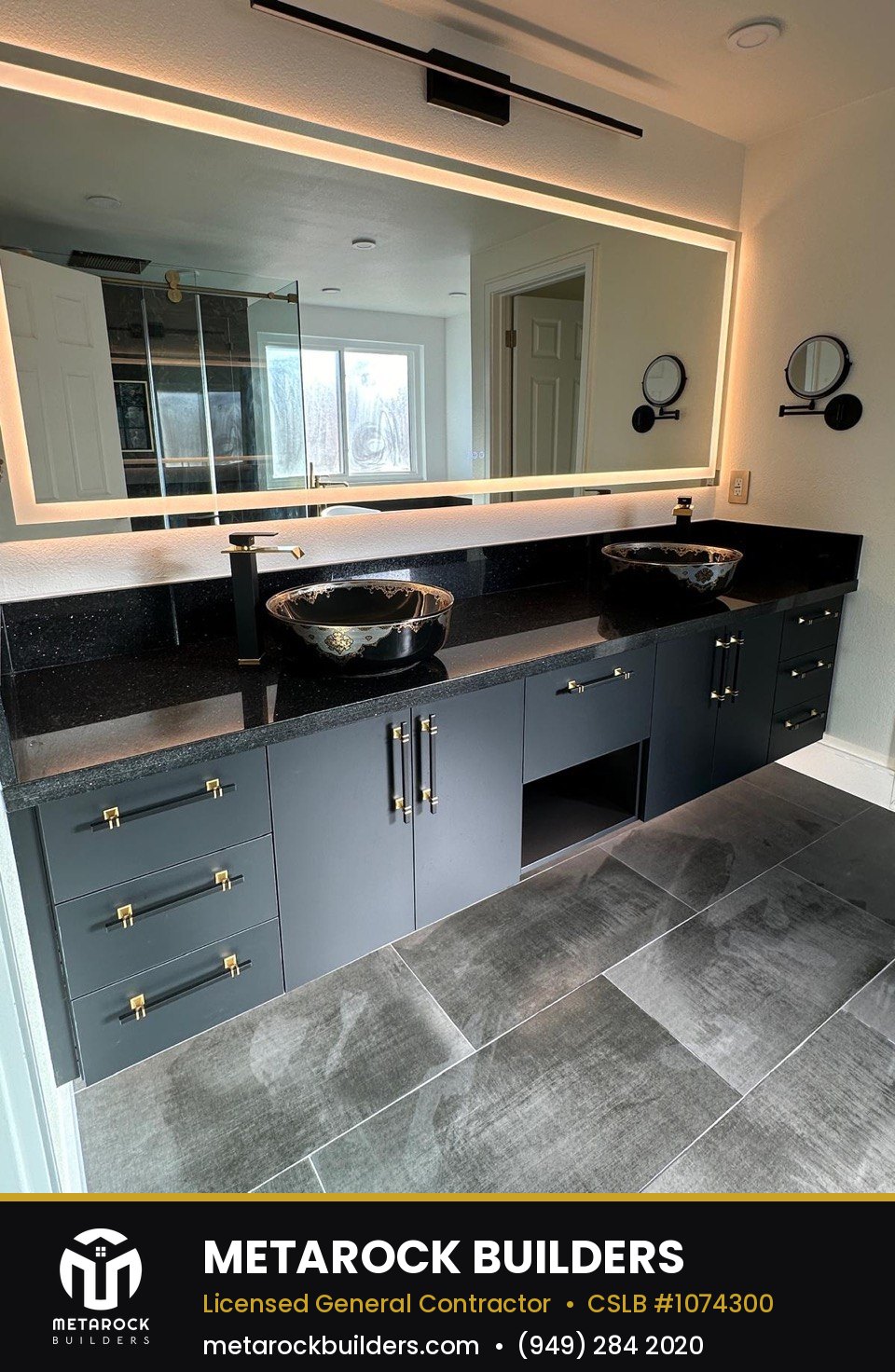 Bathroom remodel in Orange County by Metarock Builders, completed after photo with navy shaker vanity, black quartz counters, vessel sinks, brushed brass hardware, and backlit LED mirror