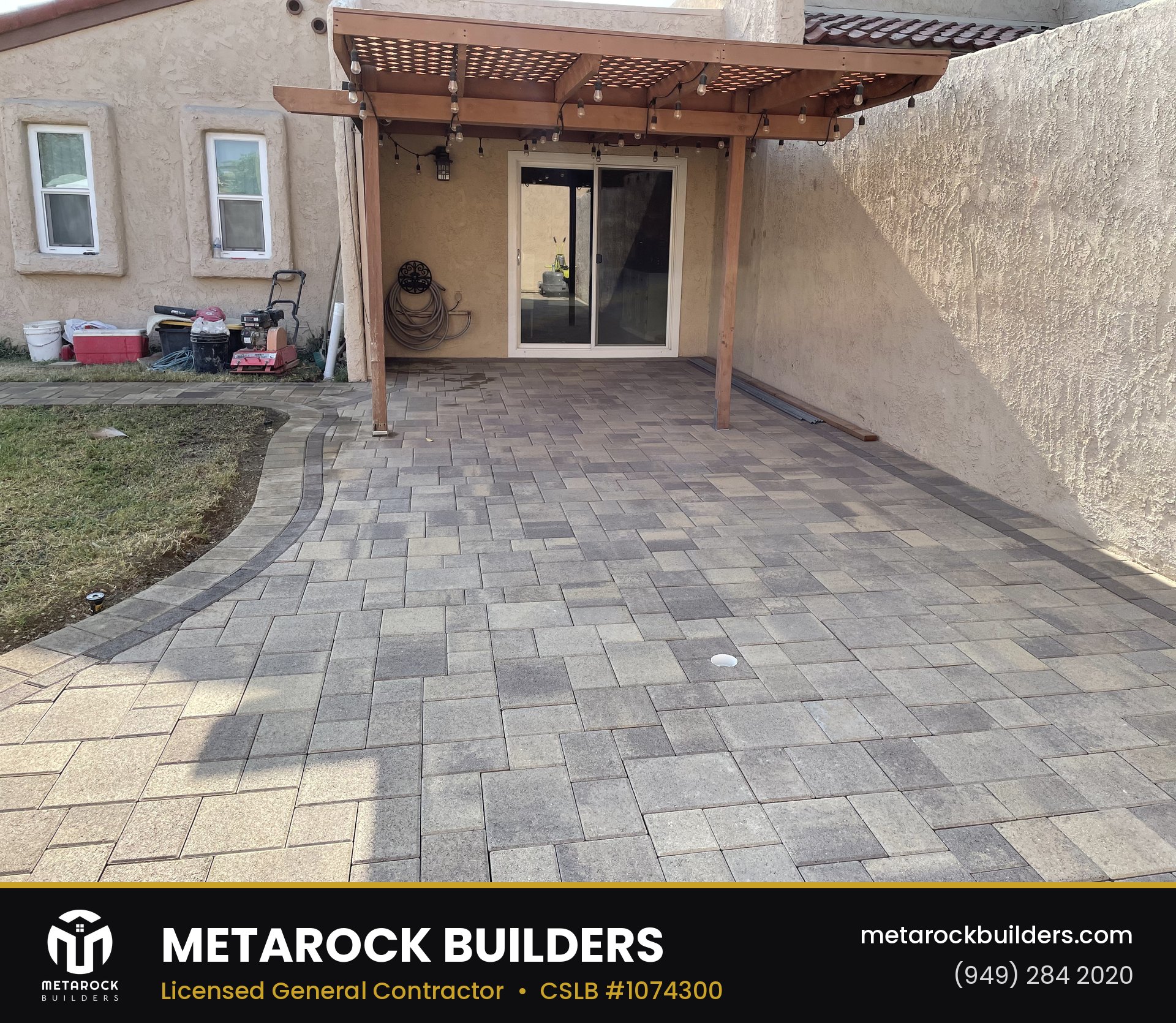 Paver patio in Orange County by Metarock Builders, completed after photo with multi-tone stone pavers, curved lawn border, wood pergola, and string lights
